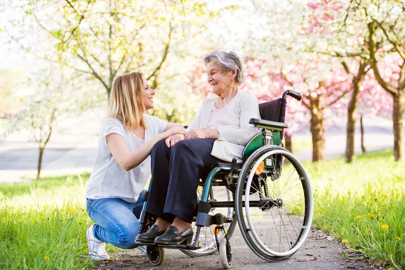 Seniorin im Rollstuhl mit ihrer Begleiterin im Frühling