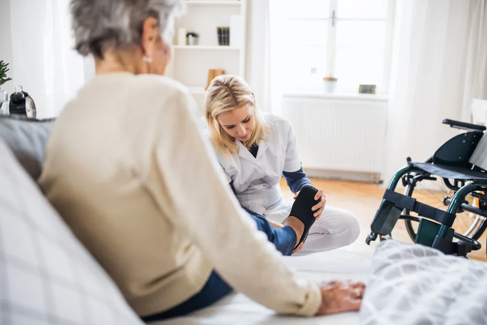 Betreuerin hilft einer Seniorin zu Hause in die Hausschuhe